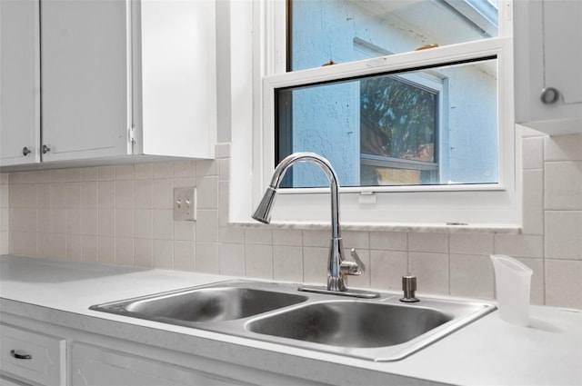 interior details featuring backsplash, white cabinets, a sink, and light countertops