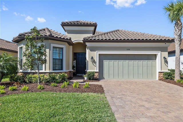 mediterranean / spanish home with stone siding, decorative driveway, an attached garage, a tile roof, and stucco siding