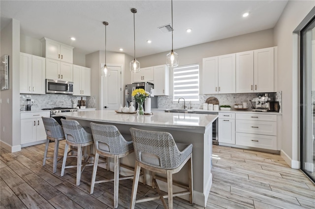 kitchen featuring a kitchen island, light wood finished floors, white cabinetry, a breakfast bar, and appliances with stainless steel finishes