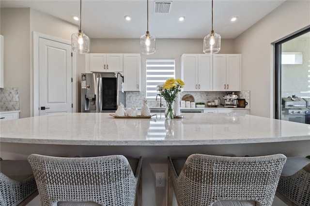 kitchen featuring white cabinets, tasteful backsplash, stainless steel refrigerator with ice dispenser, and a large island