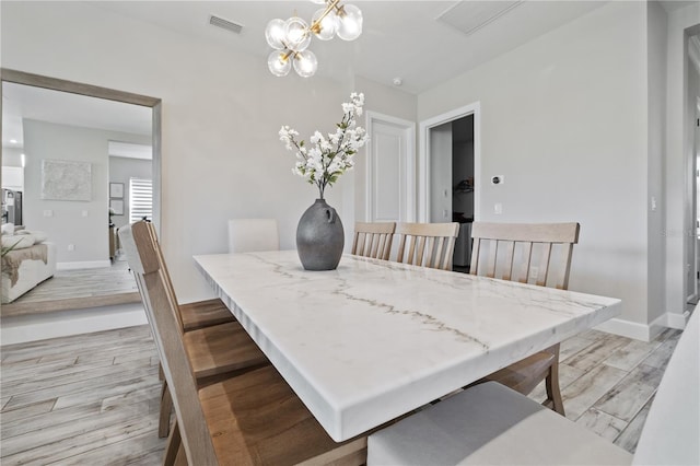 dining area featuring light wood-style flooring, baseboards, a chandelier, and visible vents