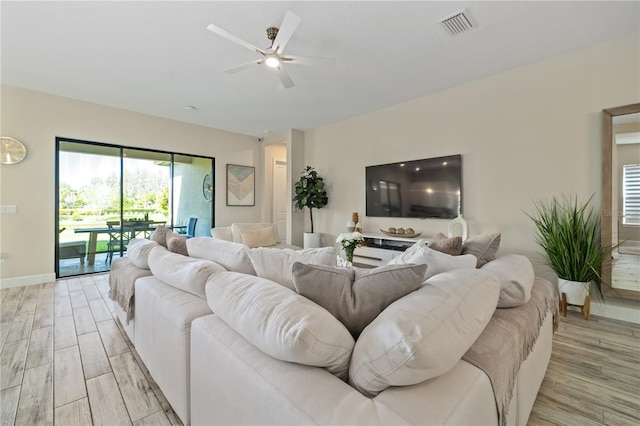 living room featuring ceiling fan, baseboards, light wood finished floors, and visible vents