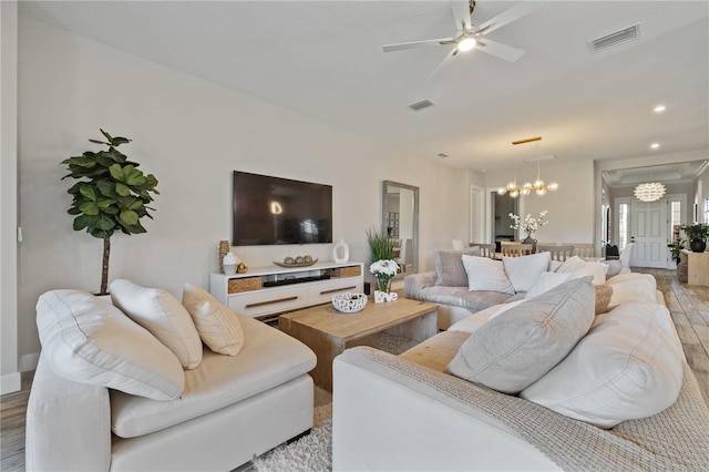 living room featuring light wood-style flooring, recessed lighting, ceiling fan with notable chandelier, and visible vents
