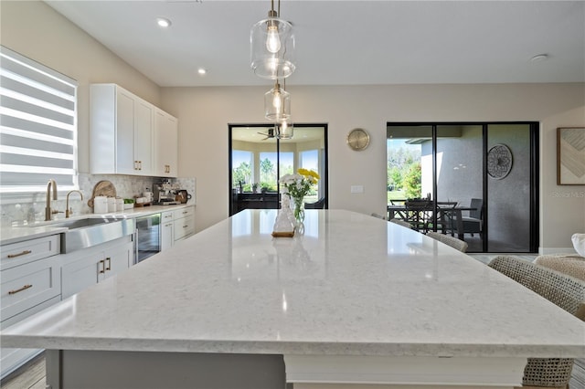 kitchen featuring white cabinetry, a spacious island, a sink, beverage cooler, and light stone countertops