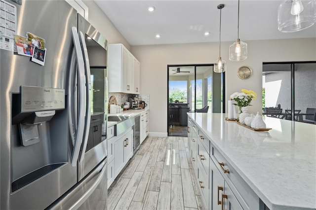 kitchen with stainless steel fridge, light wood finished floors, light stone countertops, white cabinetry, and backsplash