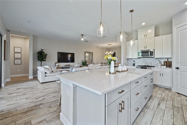 kitchen featuring light wood-style flooring, stainless steel microwave, ceiling fan with notable chandelier, white cabinets, and decorative backsplash