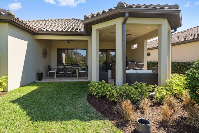 rear view of property featuring a tiled roof, stucco siding, a patio area, and a yard