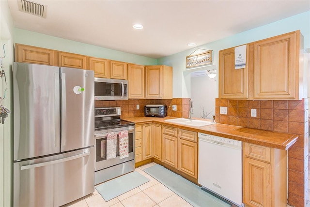 700 16th St NW, Largo, FL 33770 - kitchen featuring light tile patterned flooring, appliances with stainless steel finishes, a sink, and light brown cabinetry