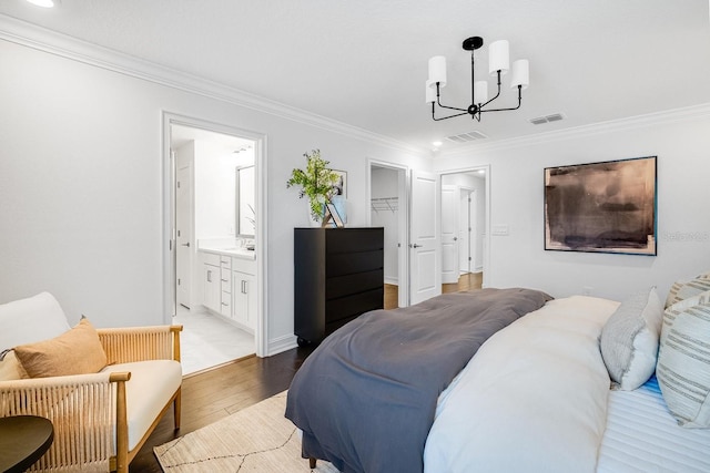 bedroom featuring visible vents, an inviting chandelier, ornamental molding, light wood-type flooring, and a walk in closet
