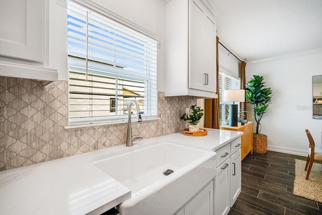kitchen with tasteful backsplash, ornamental molding, light countertops, white cabinets, and a sink