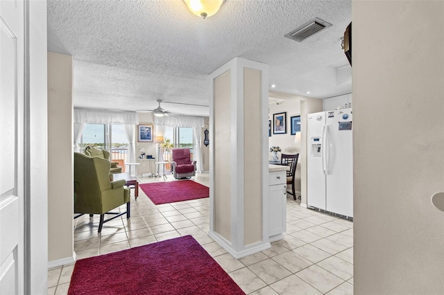 hallway featuring light tile patterned floors, a textured ceiling, baseboards, and visible vents