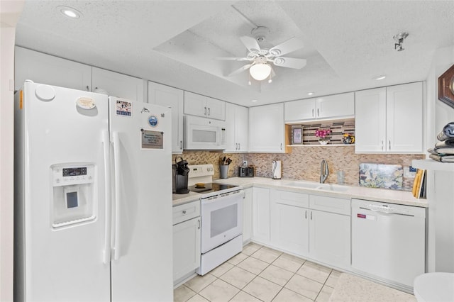 kitchen featuring light countertops, white cabinets, white appliances, a sink, and a tray ceiling