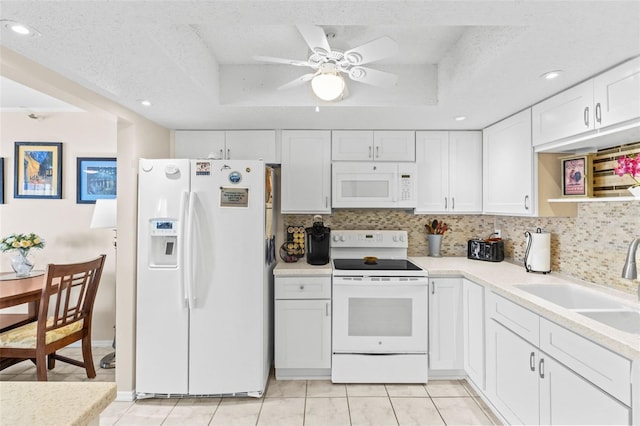 kitchen with a tray ceiling, a sink, backsplash, and white appliances