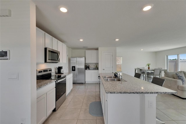 kitchen with light tile patterned floors, open floor plan, white cabinets, stainless steel appliances, and a sink