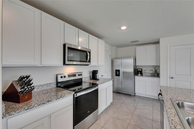 kitchen featuring visible vents, white cabinets, light tile patterned floors, appliances with stainless steel finishes, and light stone countertops
