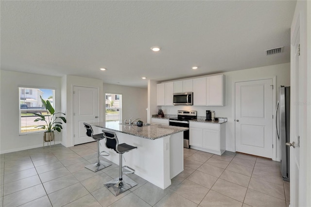 kitchen with visible vents, light stone counters, light tile patterned flooring, a sink, and stainless steel appliances