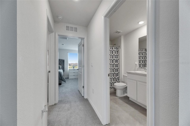 corridor featuring visible vents, baseboards, and light carpet