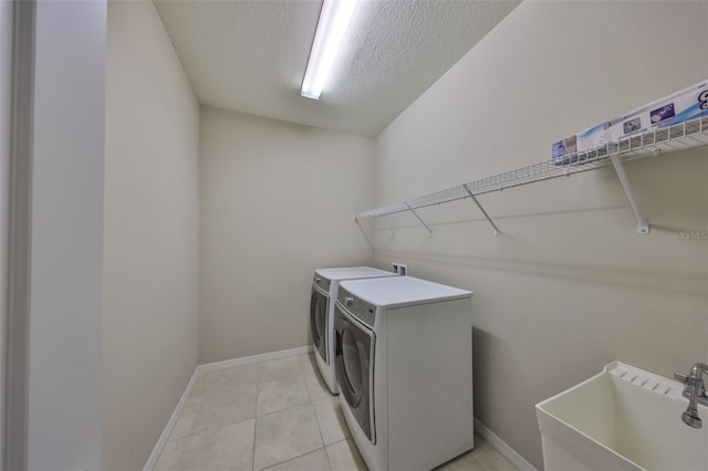 clothes washing area with washing machine and clothes dryer, laundry area, a sink, a textured ceiling, and baseboards