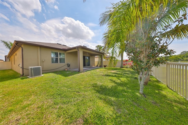 rear view of house with a patio, a fenced backyard, stucco siding, central AC unit, and a yard