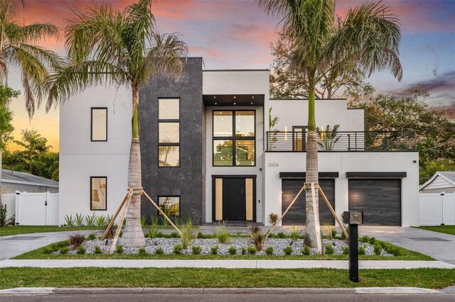 contemporary house with a balcony, fence, a garage, stucco siding, and driveway