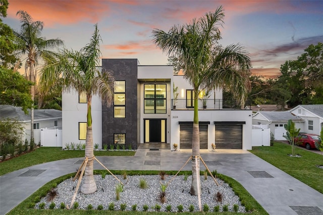 contemporary home featuring a balcony, a gate, fence, concrete driveway, and stucco siding