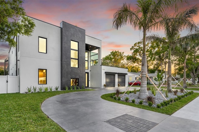 contemporary home with curved driveway, stucco siding, fence, a lawn, and a garage
