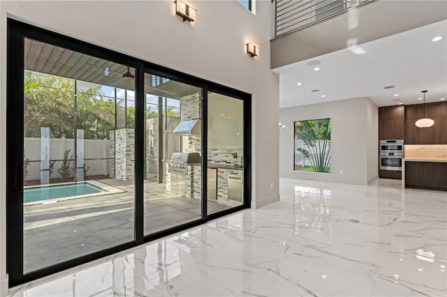 doorway to outside featuring marble finish floor, baseboards, a high ceiling, and recessed lighting