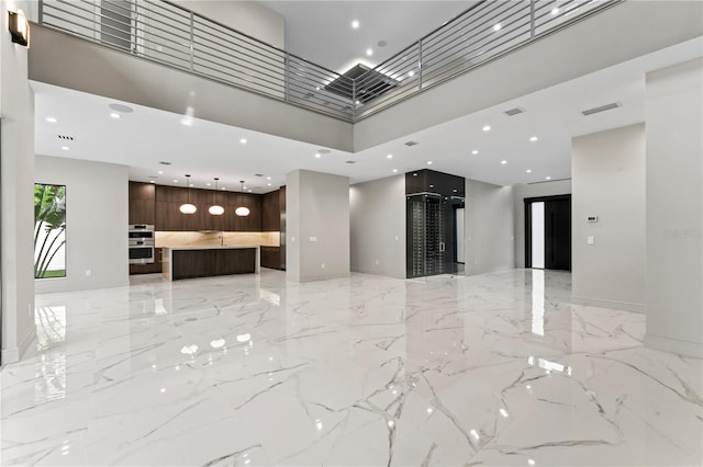 unfurnished living room with marble finish floor, visible vents, a high ceiling, and recessed lighting