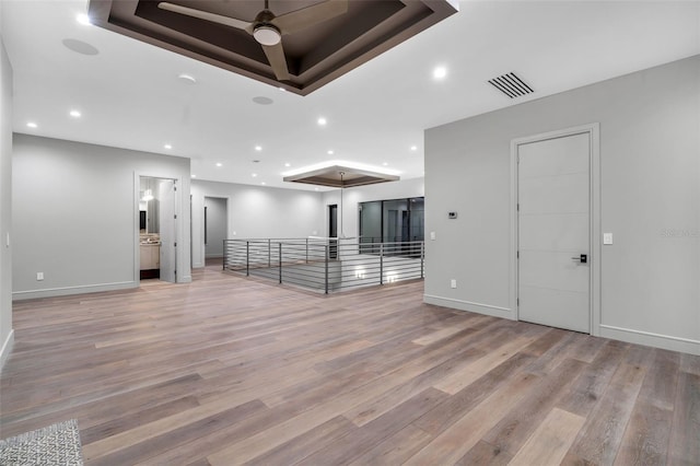 unfurnished room with visible vents, a ceiling fan, light wood-style floors, and a raised ceiling