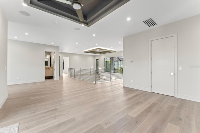 empty room featuring light wood-style flooring, a tray ceiling, visible vents, and recessed lighting