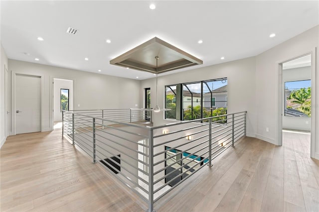 corridor featuring a wealth of natural light, visible vents, light wood-style flooring, and a raised ceiling