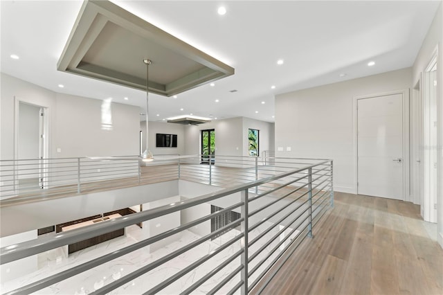 corridor with an upstairs landing, recessed lighting, light wood-type flooring, and a raised ceiling