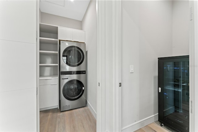 laundry room featuring wine cooler, stacked washer / drying machine, light wood-type flooring, laundry area, and baseboards