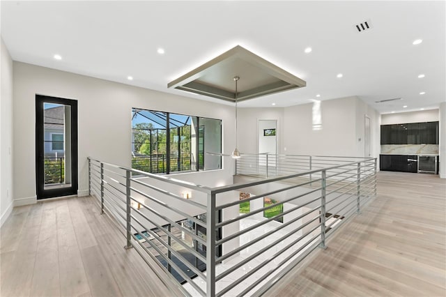 hall featuring recessed lighting, a tray ceiling, light wood-style floors, and visible vents