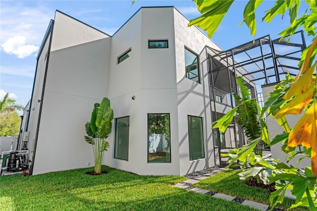 view of side of home featuring glass enclosure, stucco siding, and a yard