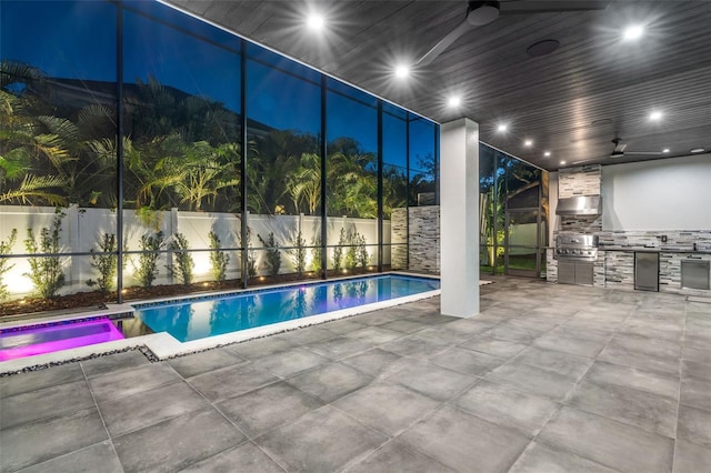 view of swimming pool featuring a ceiling fan, exterior kitchen, glass enclosure, and a patio area