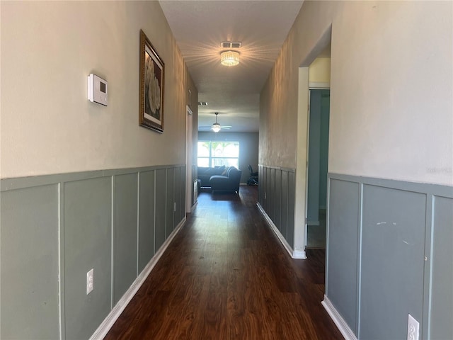hall with a decorative wall, wainscoting, and dark wood-style floors