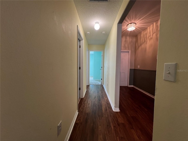 corridor with wood finished floors, baseboards, and a textured ceiling