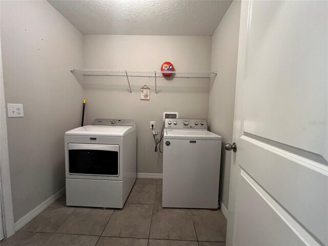 laundry area featuring washing machine and dryer, light tile patterned flooring, a textured ceiling, and baseboards