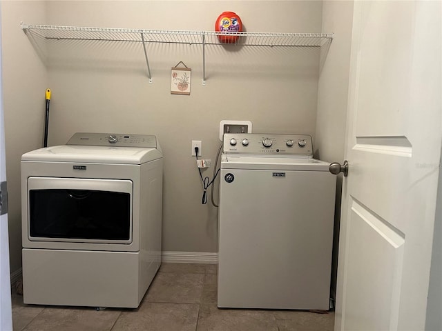 clothes washing area with washing machine and clothes dryer, light tile patterned floors, and baseboards