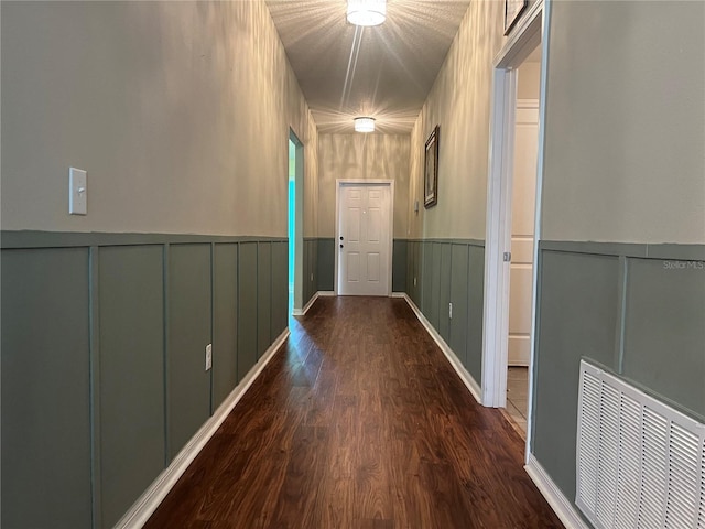 corridor with dark wood-style floors, a wainscoted wall, and a decorative wall