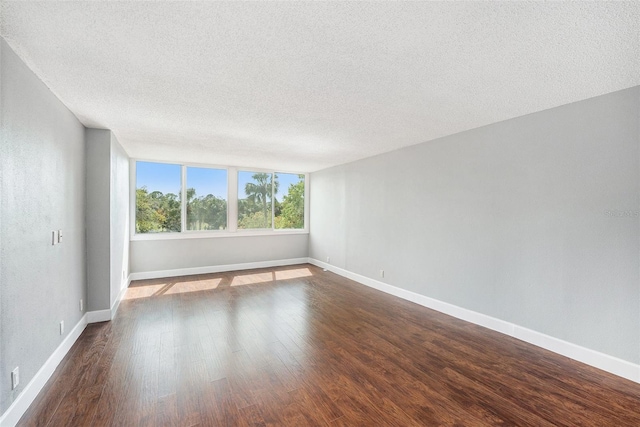 spare room featuring dark wood-style flooring, baseboards, and a textured ceiling