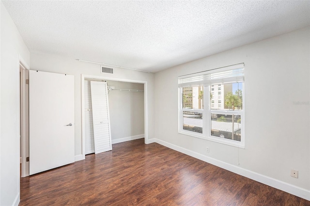 unfurnished bedroom with a closet, a textured ceiling, visible vents, baseboards, and wood finished floors
