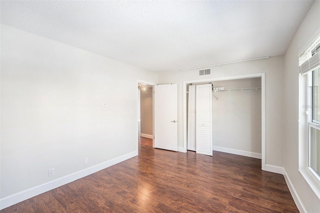 unfurnished bedroom featuring dark wood-style floors, visible vents, a closet, and baseboards