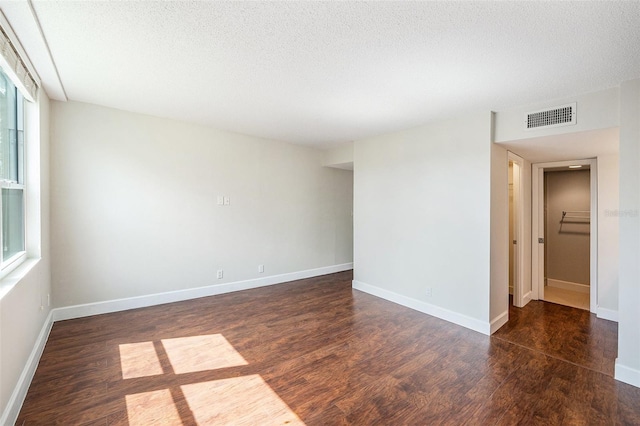 empty room featuring wood finished floors, a textured ceiling, baseboards, and visible vents