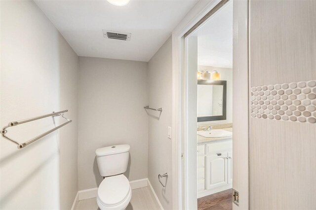 bathroom with visible vents, baseboards, toilet, wood finished floors, and vanity