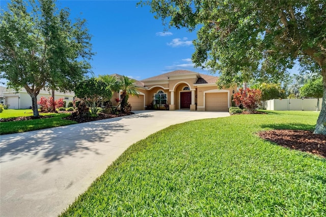 mediterranean / spanish-style home featuring stucco siding, a front yard, fence, an attached garage, and driveway
