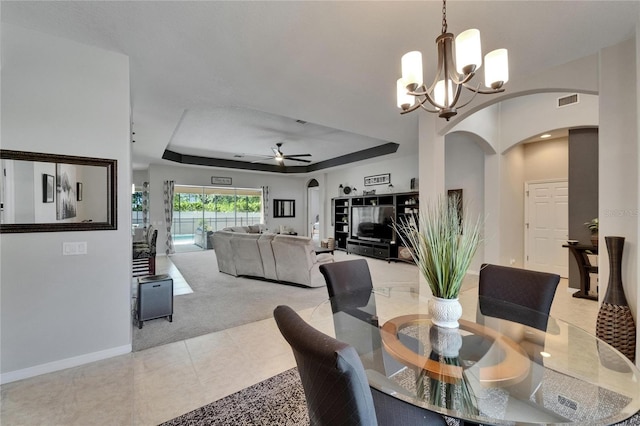 dining room featuring ceiling fan with notable chandelier, a tray ceiling, arched walkways, light tile patterned flooring, and baseboards