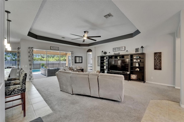 carpeted living room with a raised ceiling, a textured ceiling, a ceiling fan, and arched walkways
