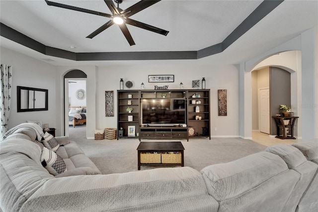 living area featuring arched walkways, ceiling fan, baseboards, and light carpet